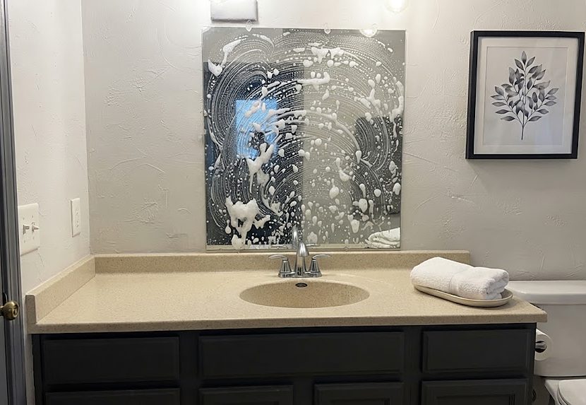 Bathroom mirror covered in cleaning foam above a wiped vanity, fresh towels set out